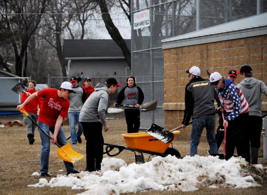 The boys of the baseball team shovel snow off of the field before their upcoming game.