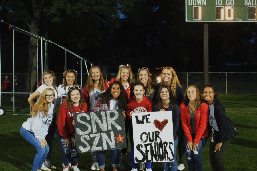 Seniors, decked out in red white and blue, Anna Giese, Macy Duden, Jada Krinke, Olivia Johnson, Kylie Wersal, Sara Twedt, Vienna Qualey, Delaney Koppmann, Kay Smith, Julia Jarvi, Emma Conway, Ellie Stodden, and Zoe Jesh cheered on the Bombers from the North end zone on September 6. This is an example of one of the first lasts for the class of 2020.