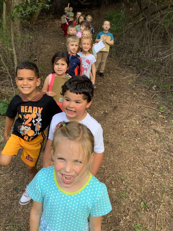 Elementary students enjoy a quick break as they hike through the woods.