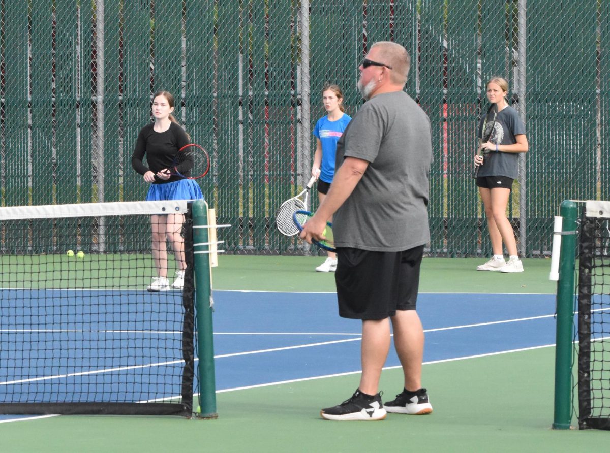 Noelle Swenson, Miranda Mandelkow, and Cameron Anderson practice groundstrokes while their coach, Paul Norstad, observes. 
